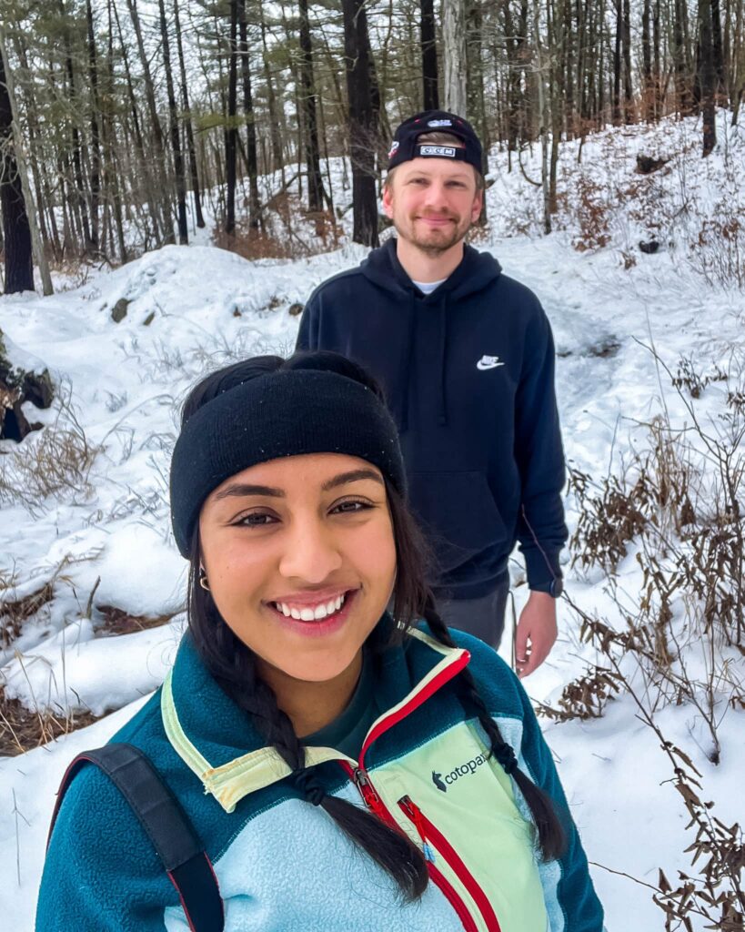 Alina and Justin snowshoeing at Frontenac Provincial Park. Alina is in the foreground smiling, Justin stands behind her.