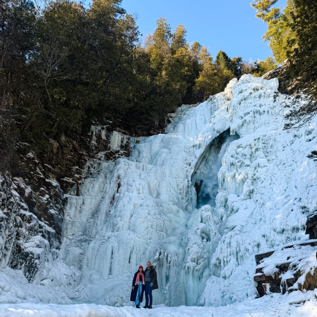A couple standing in front of a frozen waterfall at Chute Jean Larose outside of Quebec City.