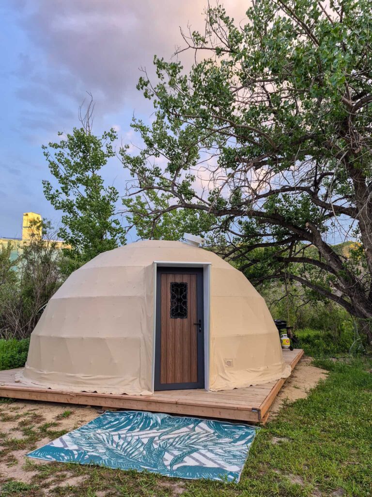 Outside view of the Rainforest Getaway Geodome. There is a half-sphere beige tent on a wooden deck.