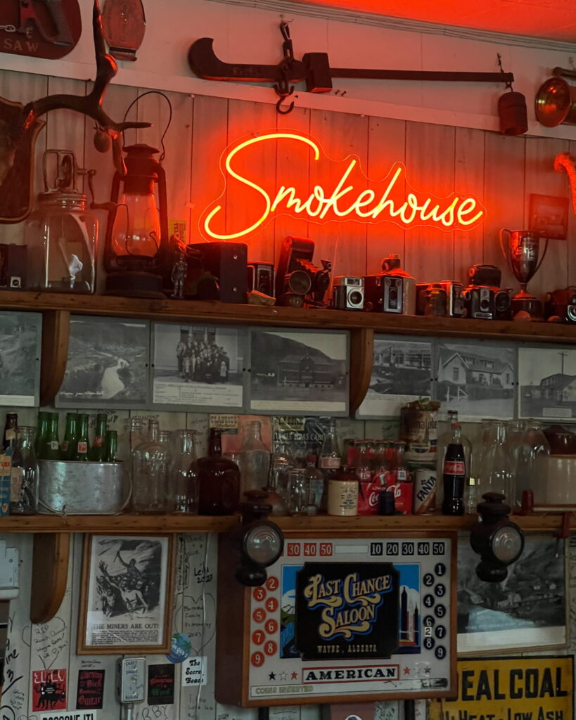 Inside the Last Chance Saloon. There is a red neon sign that says "Smokehouse" and several antique objects like guns, old cameras, and glass coke bottles.