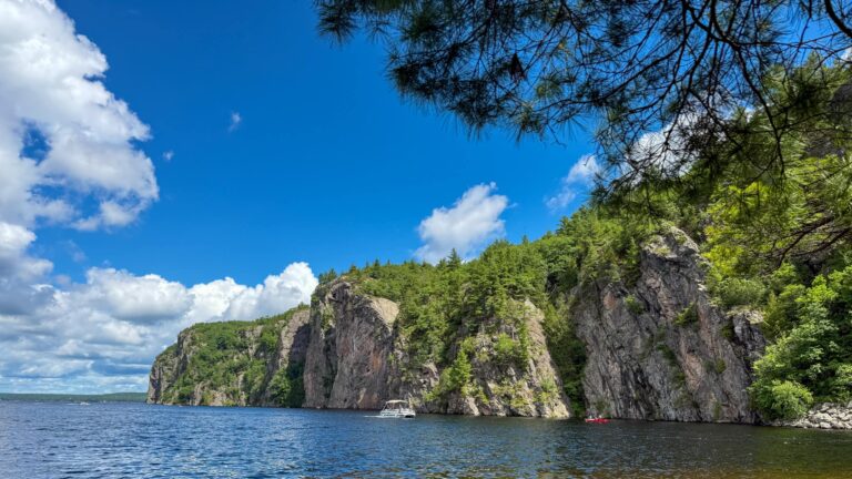 Mazinaw Rock from the Narrows. The cliff face extends along Mazinaw Lake and boats pass by.