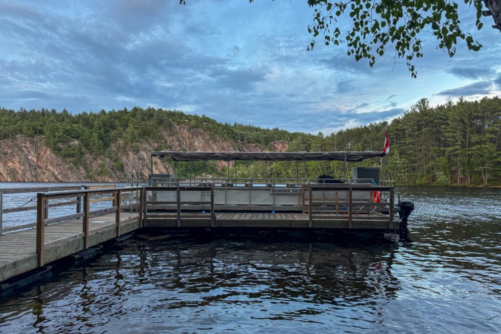 A wooden dock extending into Mazinaw Lake. There is a pontoon boat used for the tour.