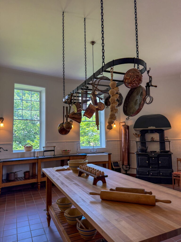 The kitchen in Boldt Castle. There are lots of counters, an antique stove in the background, and pots and pans hanging from the ceiling.